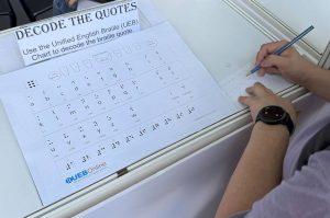 A visitor at iC2 booth takes on the challenge of decoding quotes using the Unified English Braille (UEB) chart
