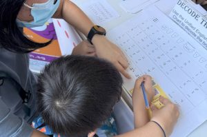 With his mother’s help, a young visitor attempts to decode a quote using the Unified English Braille (UEB) chart