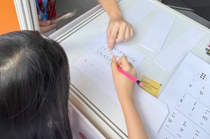 With the help of an iC2 volunteer, a young participant attempts to decode a quote using the Unified English Braille (UEB) chart