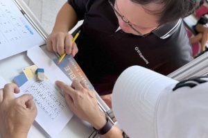 With the help of an iC2 volunteer, a visitor attempts to decode a quote using the Unified English Braille (UEB) chart