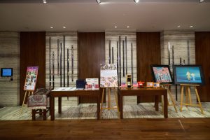 Display of raffle prizes and silent auction items, including (from left to right): Peranakan Culinary Experience with PasirPanjangBoy, 2002 Carruades de Lafite Pauillac (3000ml), Sumo – Kamala Red (Welcome) by Arnaud Nazare-Aga, The Dense Forests 密林物语 by Wu Qiong (Edition 4/88), and It's Here 在这里 by Wu Qiong (Edition 49/88)
