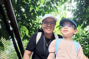 Mother and child exploring nature at the zoo, standing on a pathway surrounded by lush green foliage