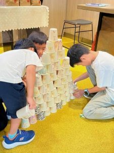 Children sitting on the floor indoors, focused on stacking cups into towers during a game.