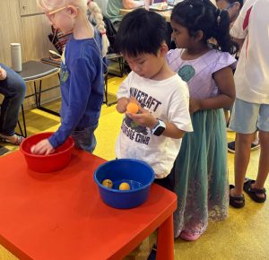 Indoor scene of excited children competing in an egg-and-spoon race.